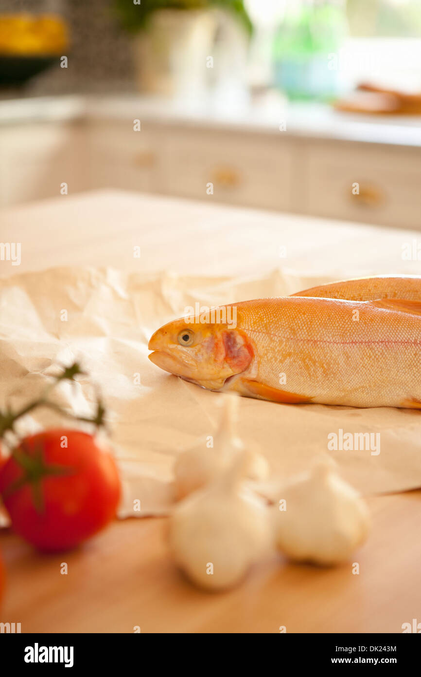 Close up di pesce intero, l'aglio ed il pomodoro di cottura Ingredienti sul banco di cucina Foto Stock