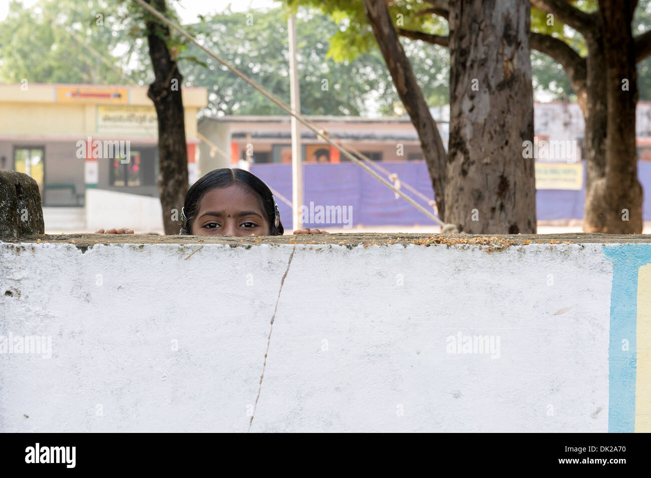 Rural Indian School girl di sbirciare da dietro il muro della scuola. Andhra Pradesh, India Foto Stock