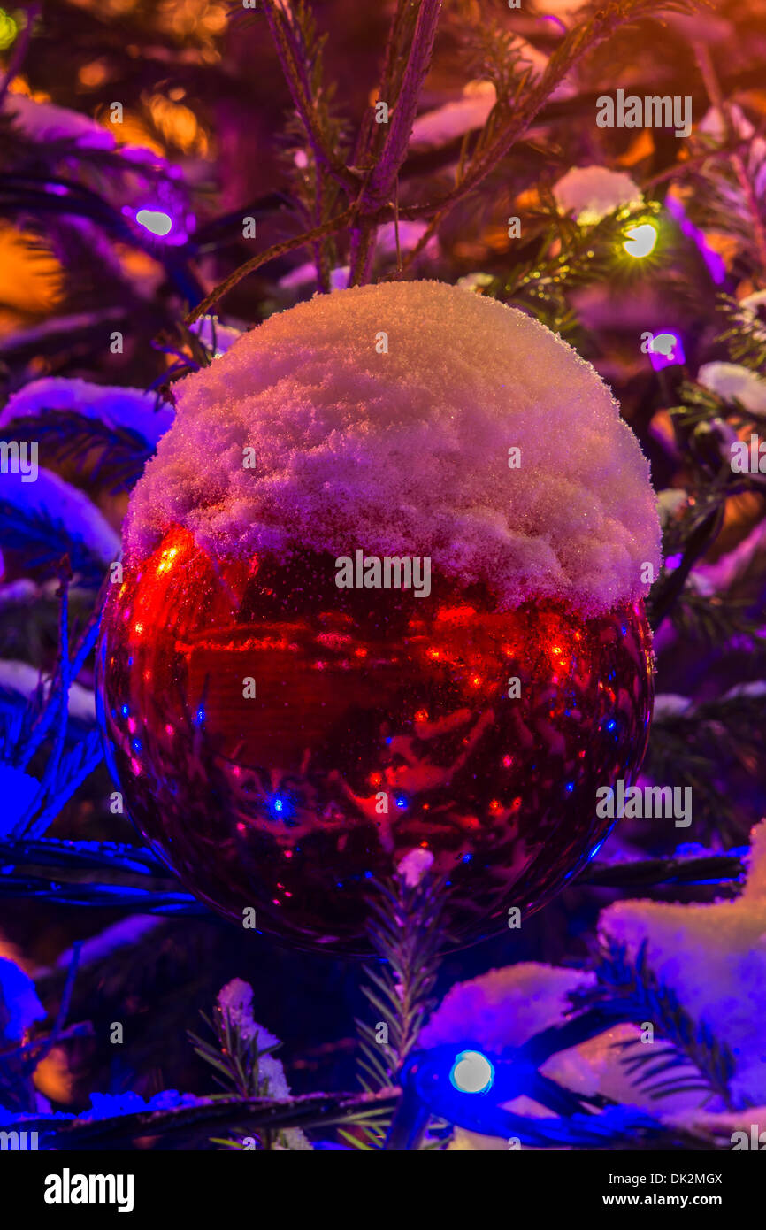 Auguri di Buon Natale. Big Red Sfera decorativa su di un albero di Natale all'aria aperta. Una tazza di neve sulla parte superiore della sfera Foto Stock