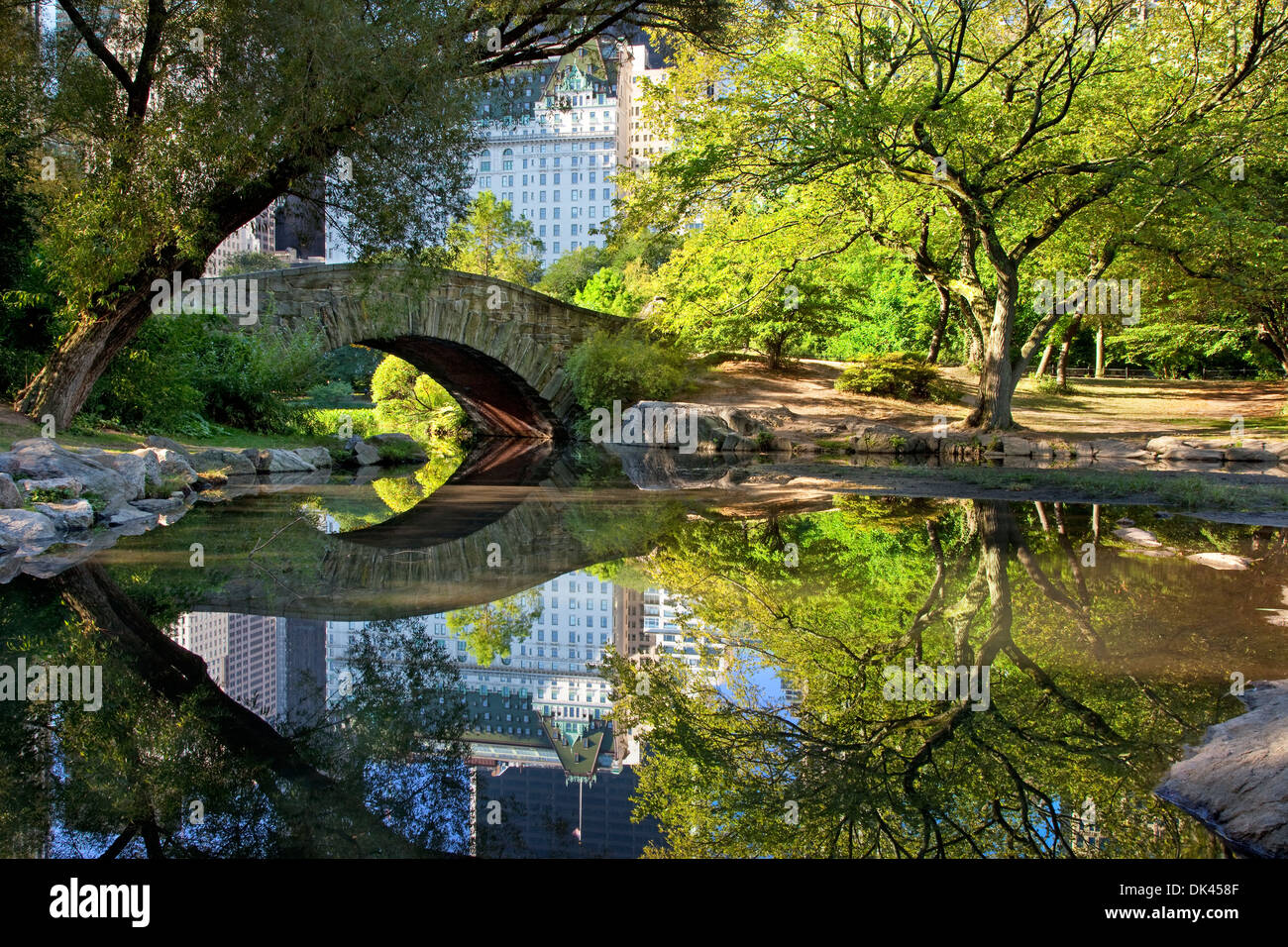 Ponte di pietra sul laghetto di Central Park con riflessioni del Plaza Hotel di New York City, Stati Uniti d'America Foto Stock