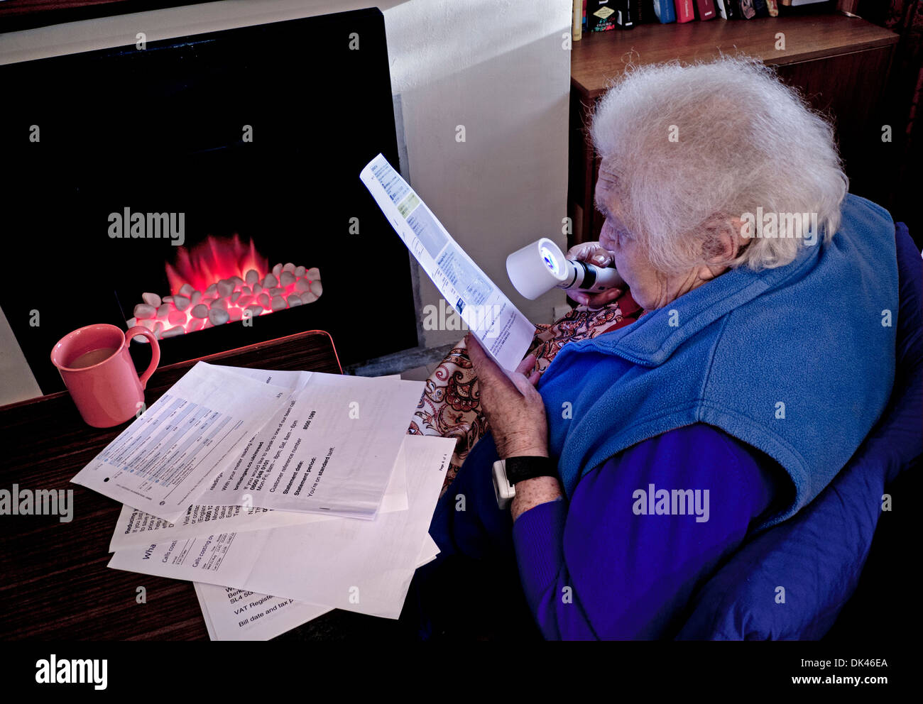Consumo di energia elettrica povertà bollette anziano indipendente 99 anni donna a casa con il fuoco a carbone utilizzando la lente di ingrandimento per leggere le bollette di energia domestica inverno Foto Stock
