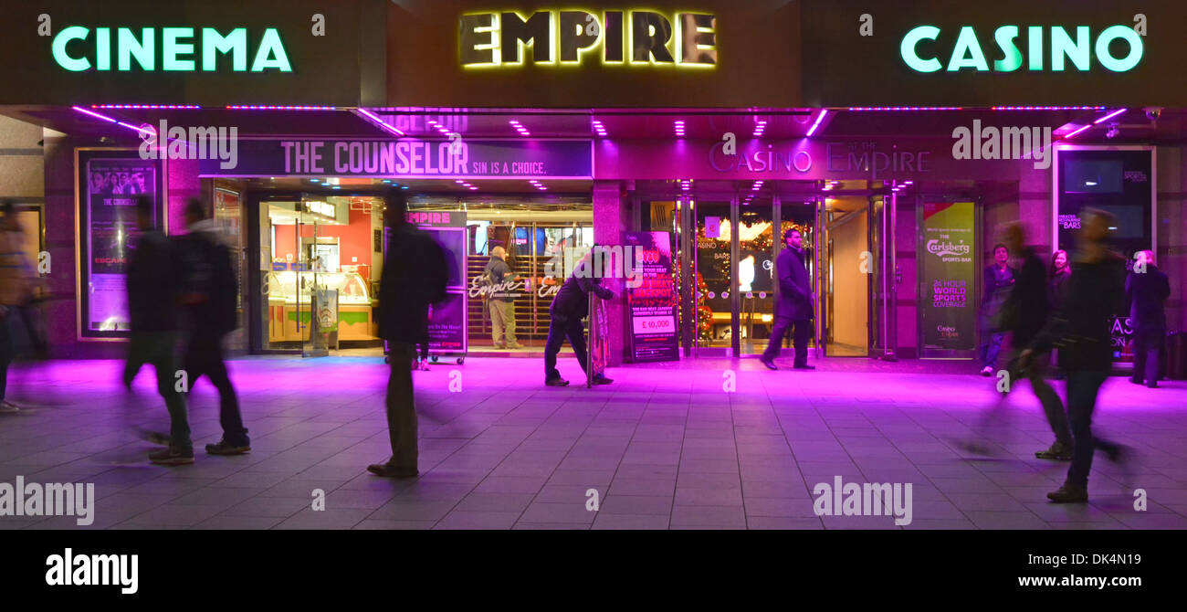 Vista serale delle persone sul marciapiede all'esterno dell'Empire Leicester Square, cinema, casinò e locali di intrattenimento, cerise illuminazione colorata delle inondazioni Londra, Inghilterra, Regno Unito Foto Stock