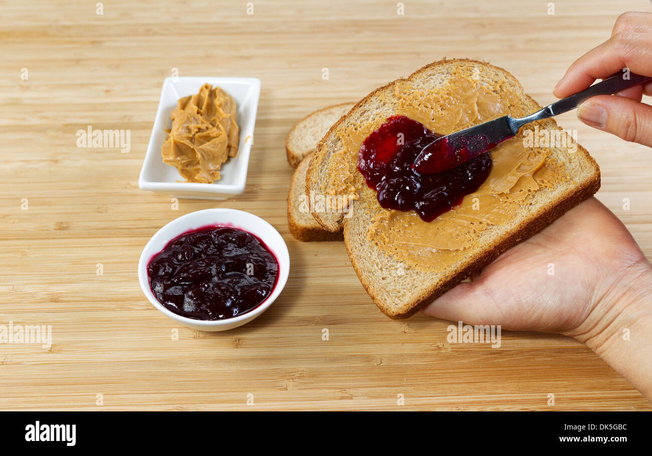 Foto orizzontale di mani femminili rendendo il burro di arachidi e jelly sandwich con bamboo naturale taglio al di sotto della scheda Foto Stock