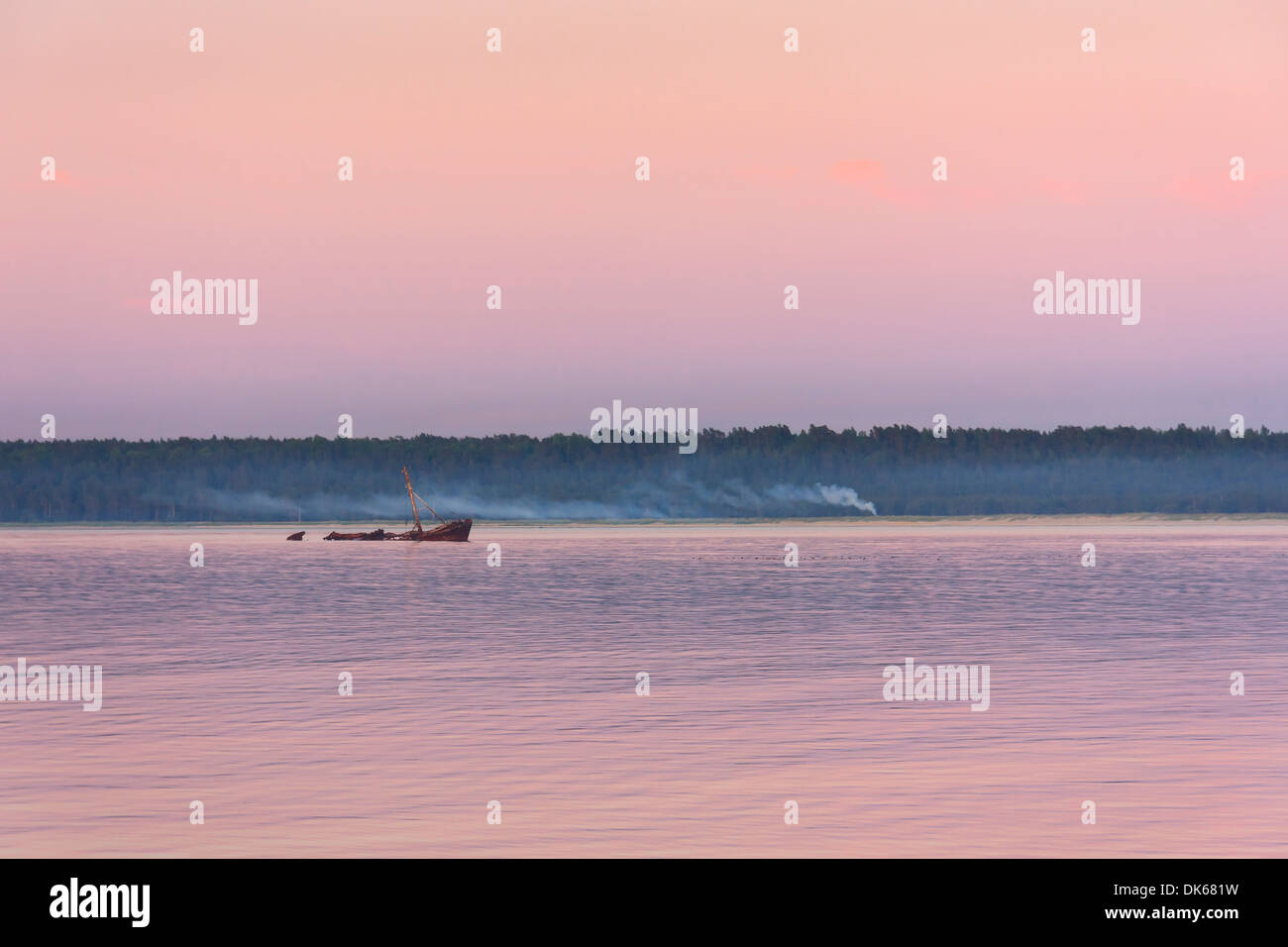 Vecchio arrugginito relitto della nave in mare in prossimità della costa viola al tramonto. Fumatori falò presso la costa. Foto Stock