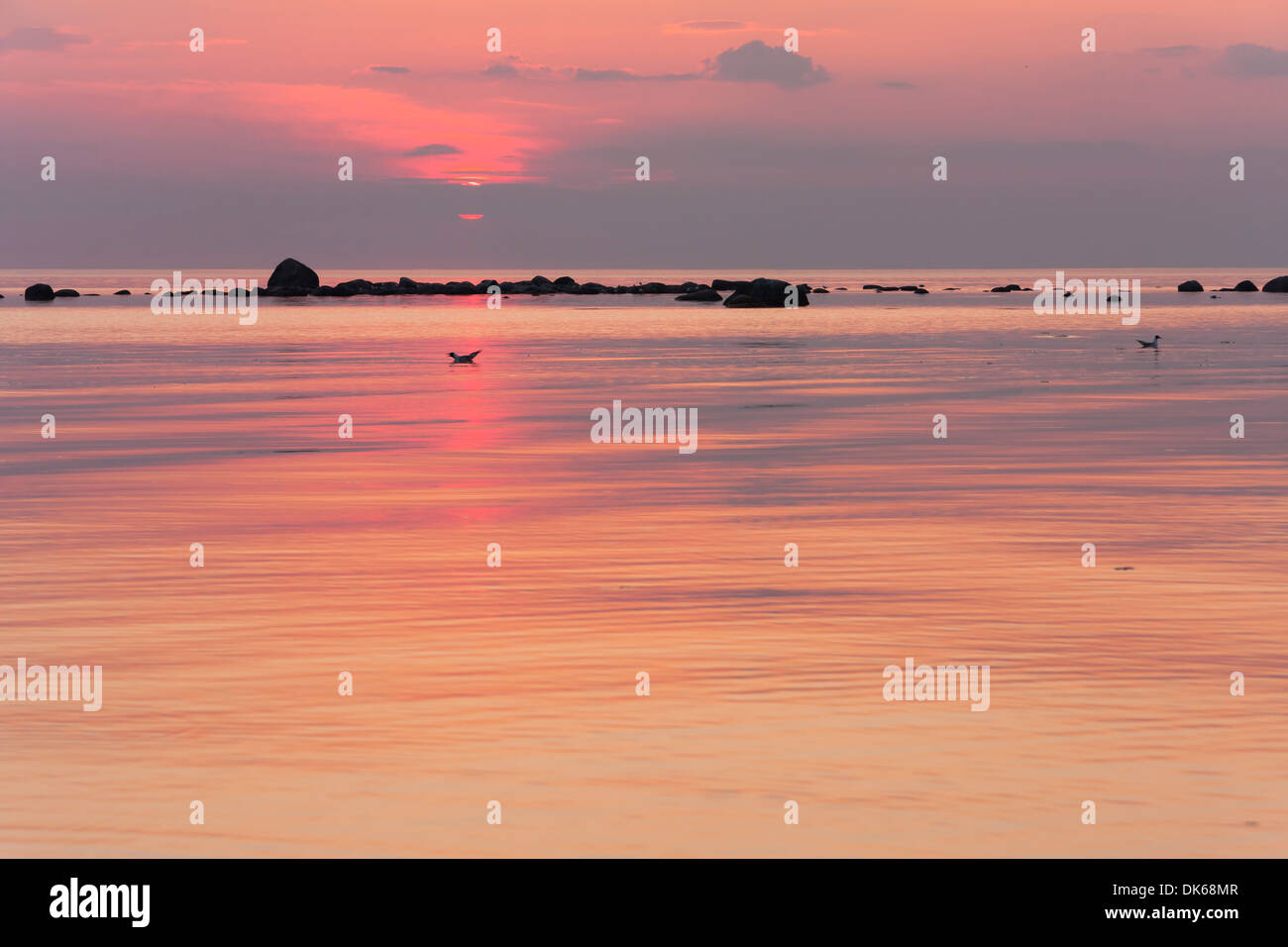 Pinky tramonto al mare, rocce in mare in background Foto Stock