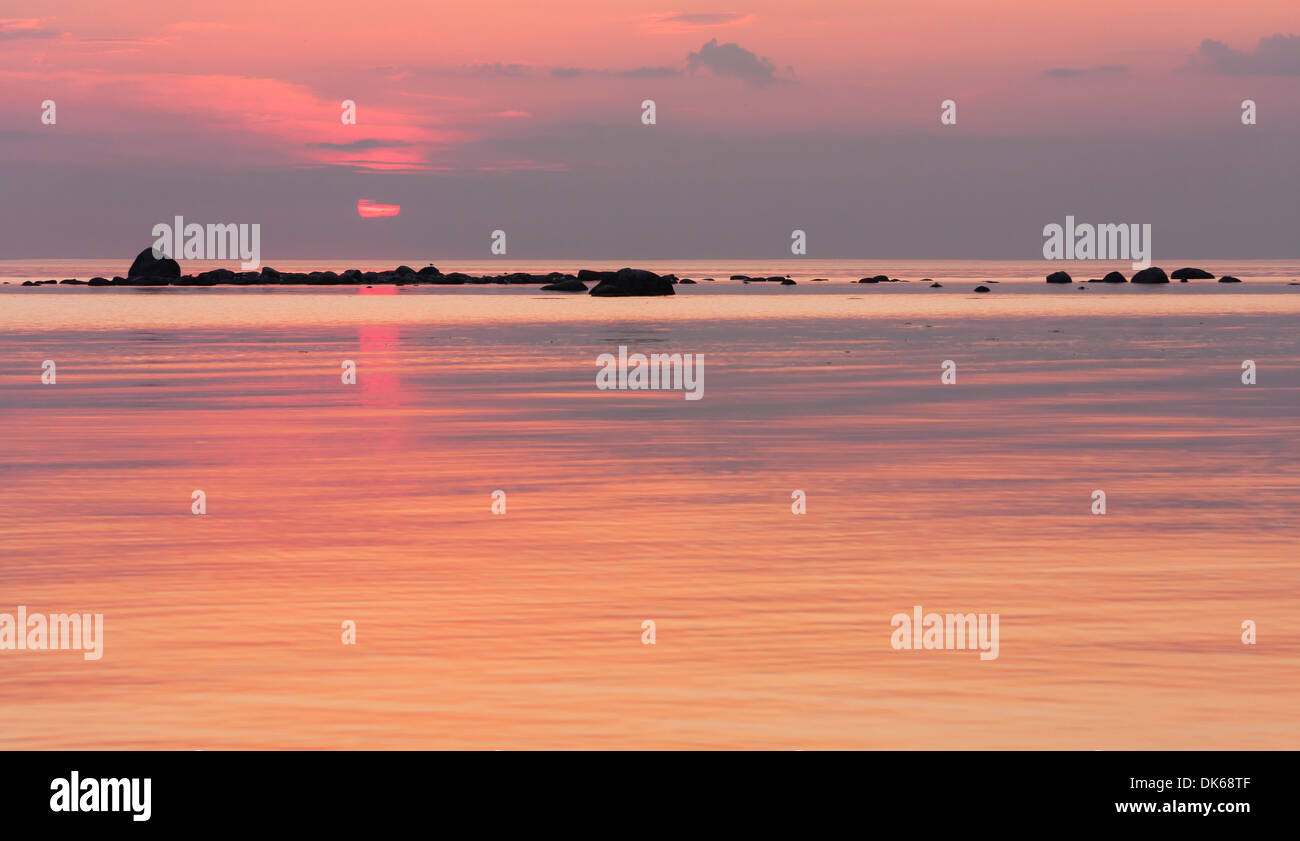 Pinky tramonto al mare, rocce in mare in background Foto Stock