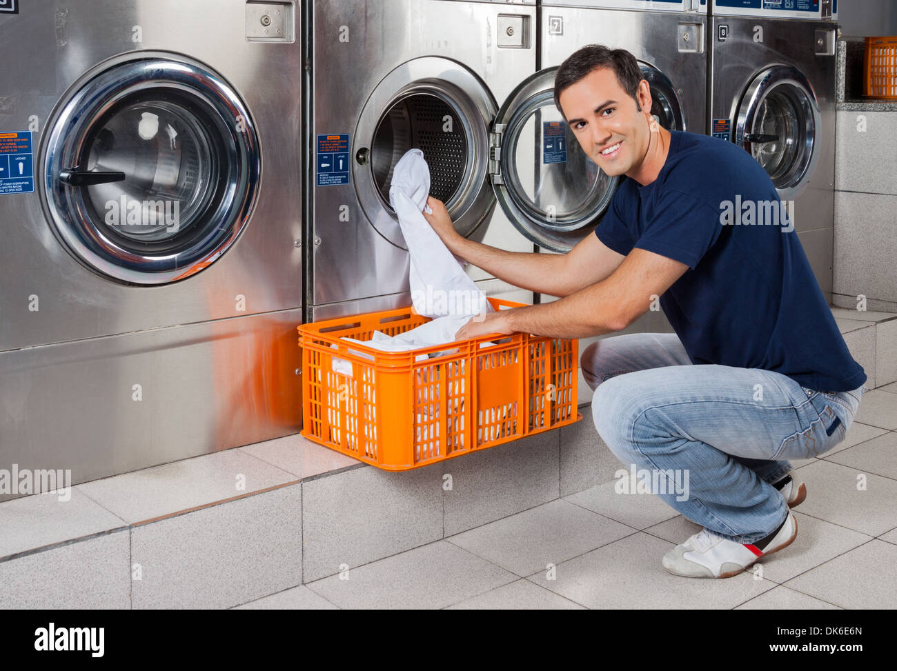 Giovane uomo di mettere i vestiti in lavatrice Foto Stock