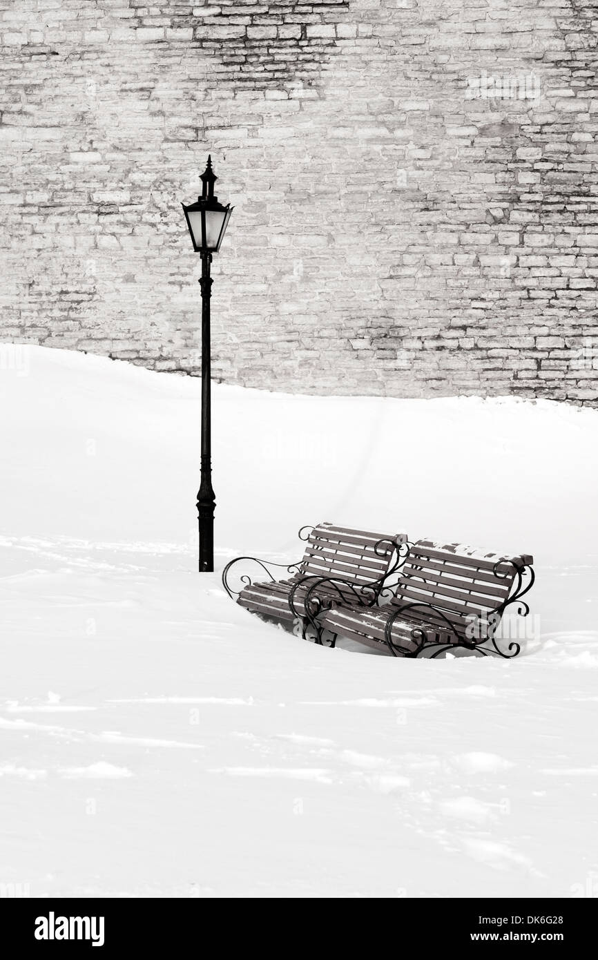 Due di legno e metallo panchine in profonda bianco della neve vicino a lanterna di strada in inverno. Muro di pietra calcarea in background. Foto Stock
