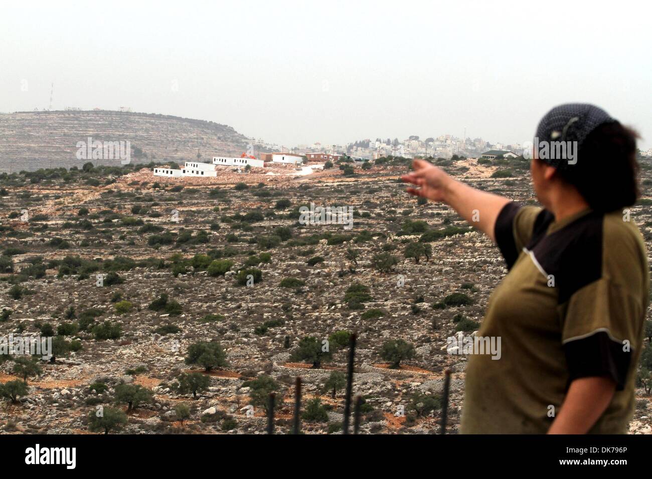 Birzeit, West Bank, Territori palestinesi. 3 Dic 2013. Una donna Palestinese dal villaggio di al-Mazraa al-Kubliyeh sembra un bungalow in distanza costruita dai coloni israeliani a un avamposto costruito sulla terra sequestrata dal villaggio palestinese, vicino la Cisgiordania città di Birzeit il 3 dicembre 2013. Il presidente palestinese Mahmud Abbas ha avvertito che continua la costruzione di insediamenti di Israele nei territori palestinesi minacciano il futuro del Medio Oriente colloqui di pace, che sono in una fase di stallo, poco più di tre mesi dopo il loro inizio (credito Immagine: © Issam Rimawi APA/images/ZUMAPRESS. Foto Stock