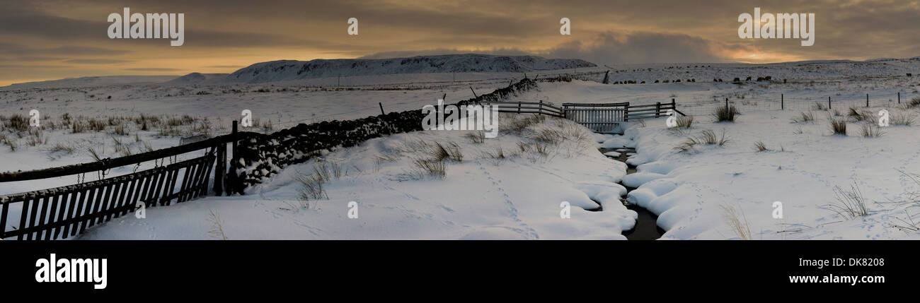 Paese scena di neve di recinzione e il flusso che conduce al colle sotto un cielo di rame Foto Stock