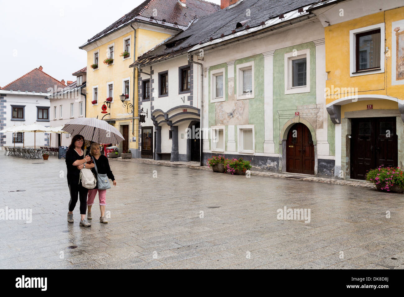 Persone con ombrellone a piedi sotto la pioggia attraverso la vecchia città di Radovljica, Slovenia Foto Stock