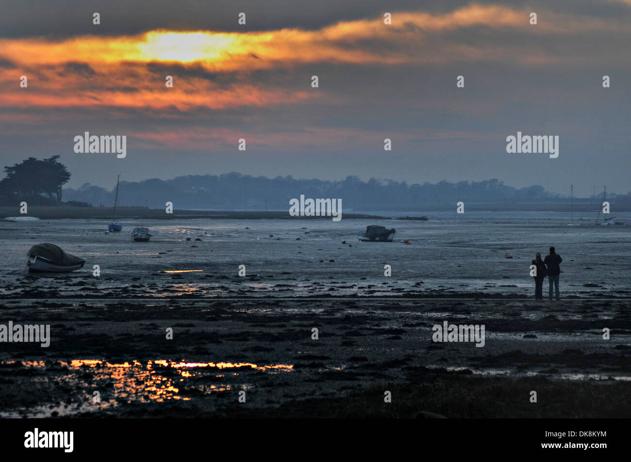 Un paio di guardare il sole invernale impostato a bassa marea su una insenatura costiera Foto Stock