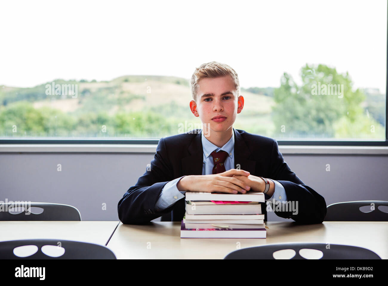 Teenage schoolboy seduto alla scrivania con la pila di libri Foto Stock