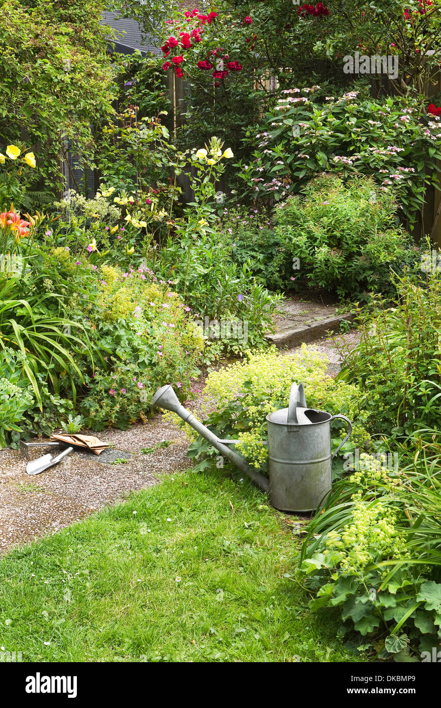 Innaffiatoio e attrezzi da giardino per la pulizia di fioritura in stile cottage garden sulla mattina d'estate - verticale Foto Stock