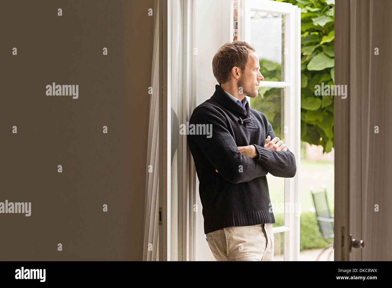 Metà uomo adulto guardando fuori della finestra, braccia incrociate Foto Stock