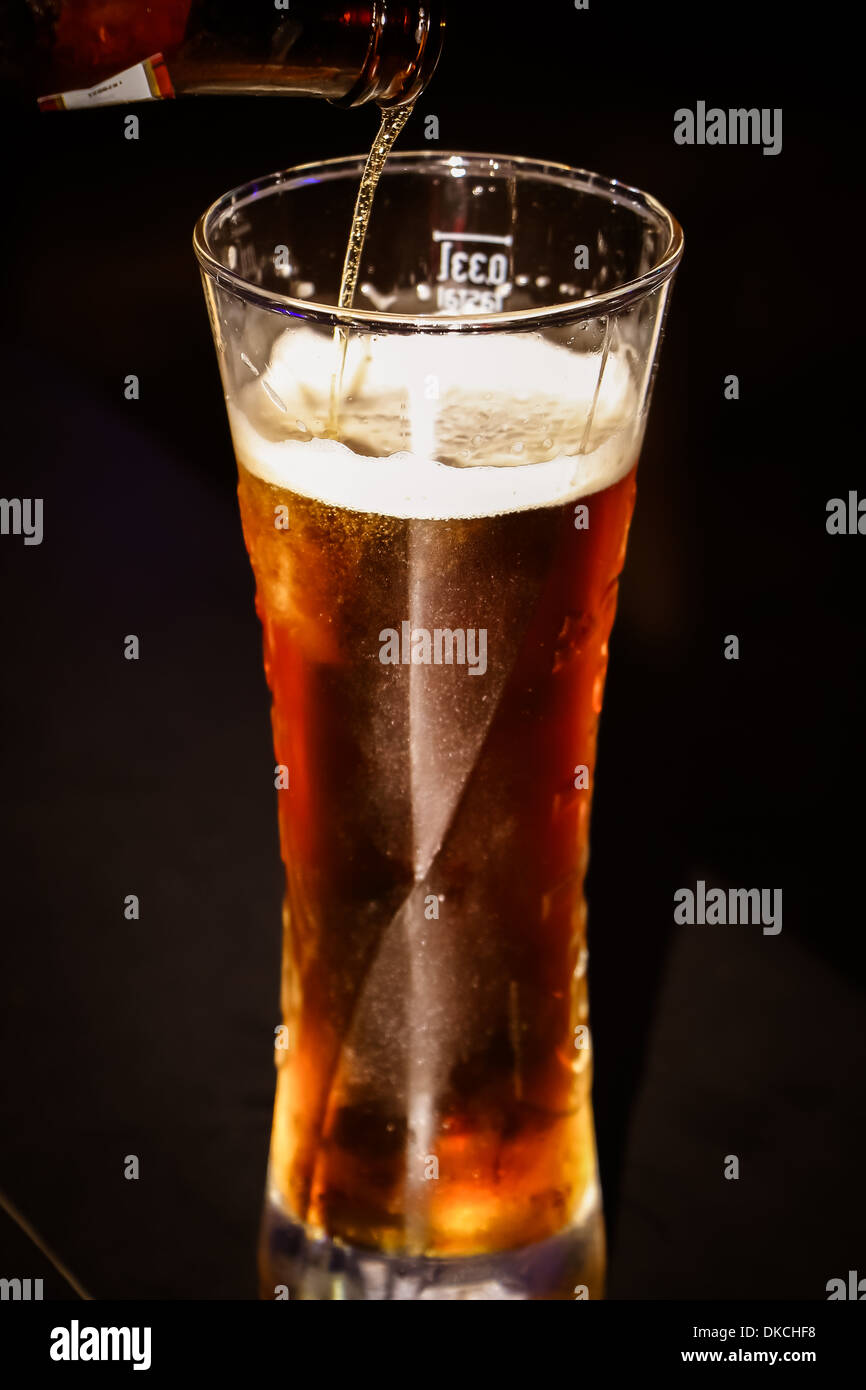 Vediamo come la birra viene versata da una bottiglia in un bicchiere Foto Stock