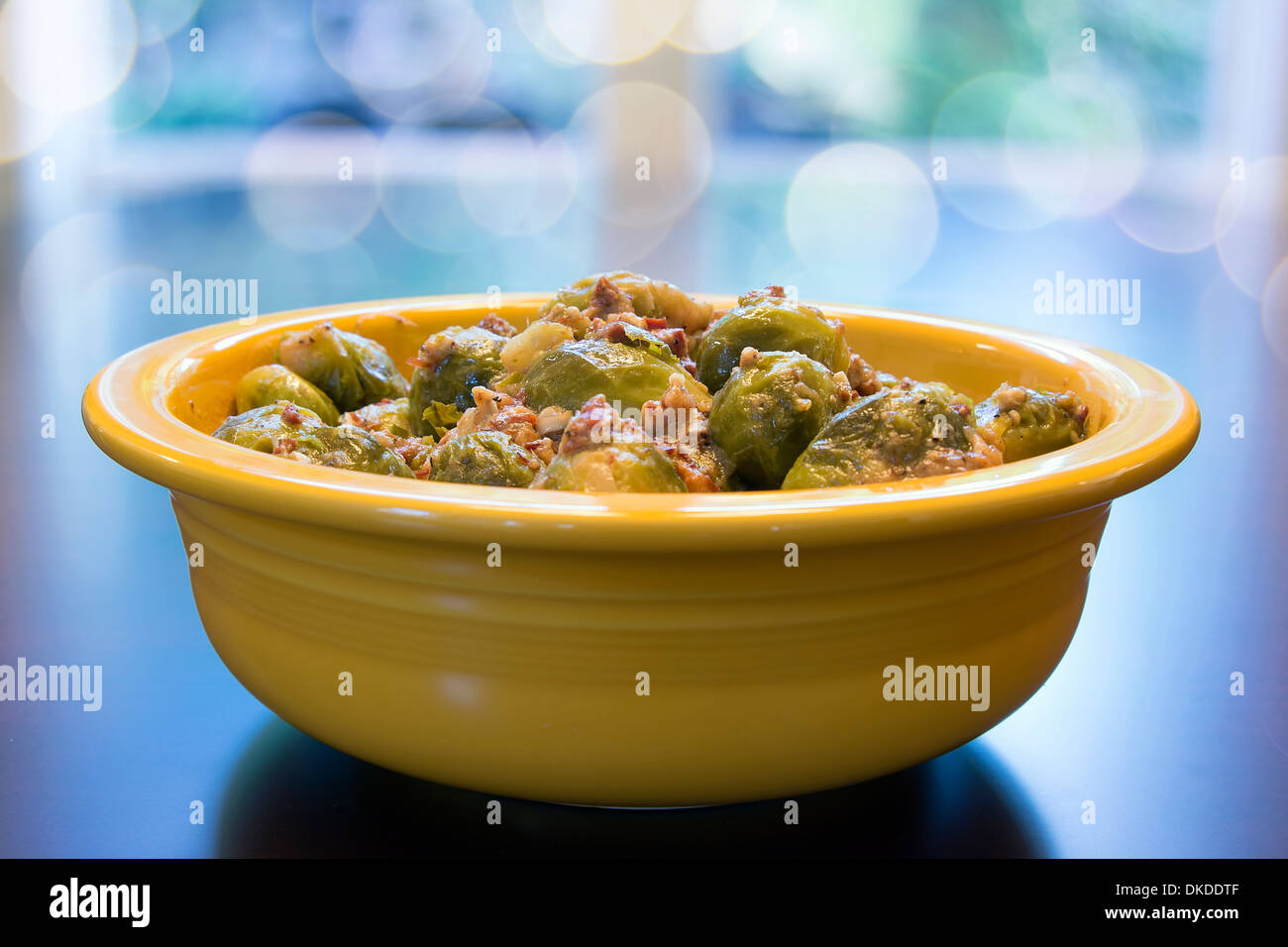 I cavoletti di Bruxelles cotti con pancetta Olio d'oliva e cipolla nel recipiente di colore giallo con Bokeh sfondo sfocato Foto Stock