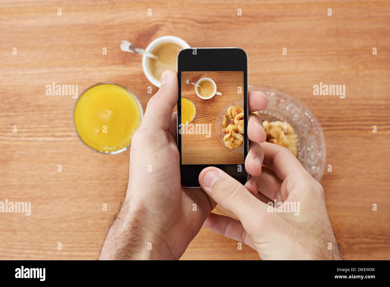 Le mani prendendo foto di prima colazione comprende cornetti, caffè e succo d'arancia con lo smartphone Foto Stock