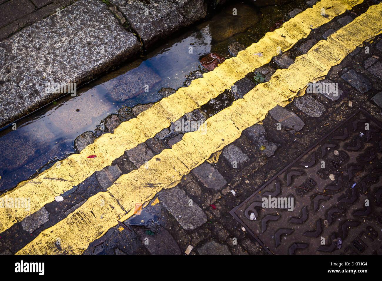 Doppie linee di colore giallo su fondo bagnato acciottolato nel nord di Londra, Inghilterra. Foto Stock