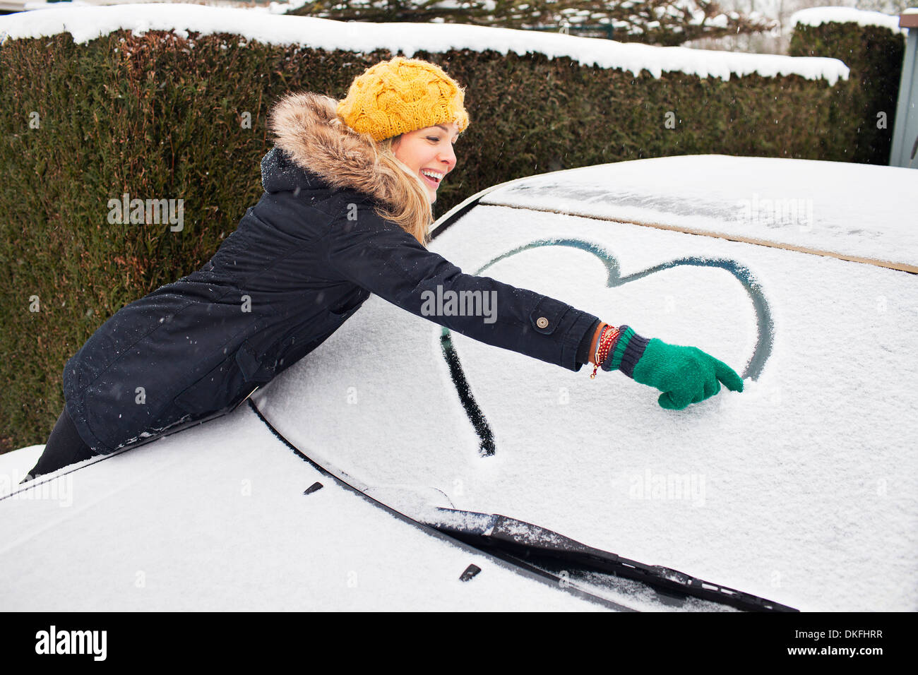 Donna disegno forma di cuore su strade coperte di neve parabrezza Foto Stock