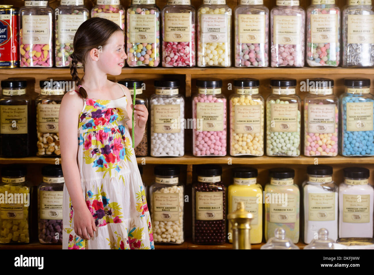 Ragazza in piedi nel negozio di dolci nella parte anteriore degli scaffali di prodotti a base di zuccheri Foto Stock