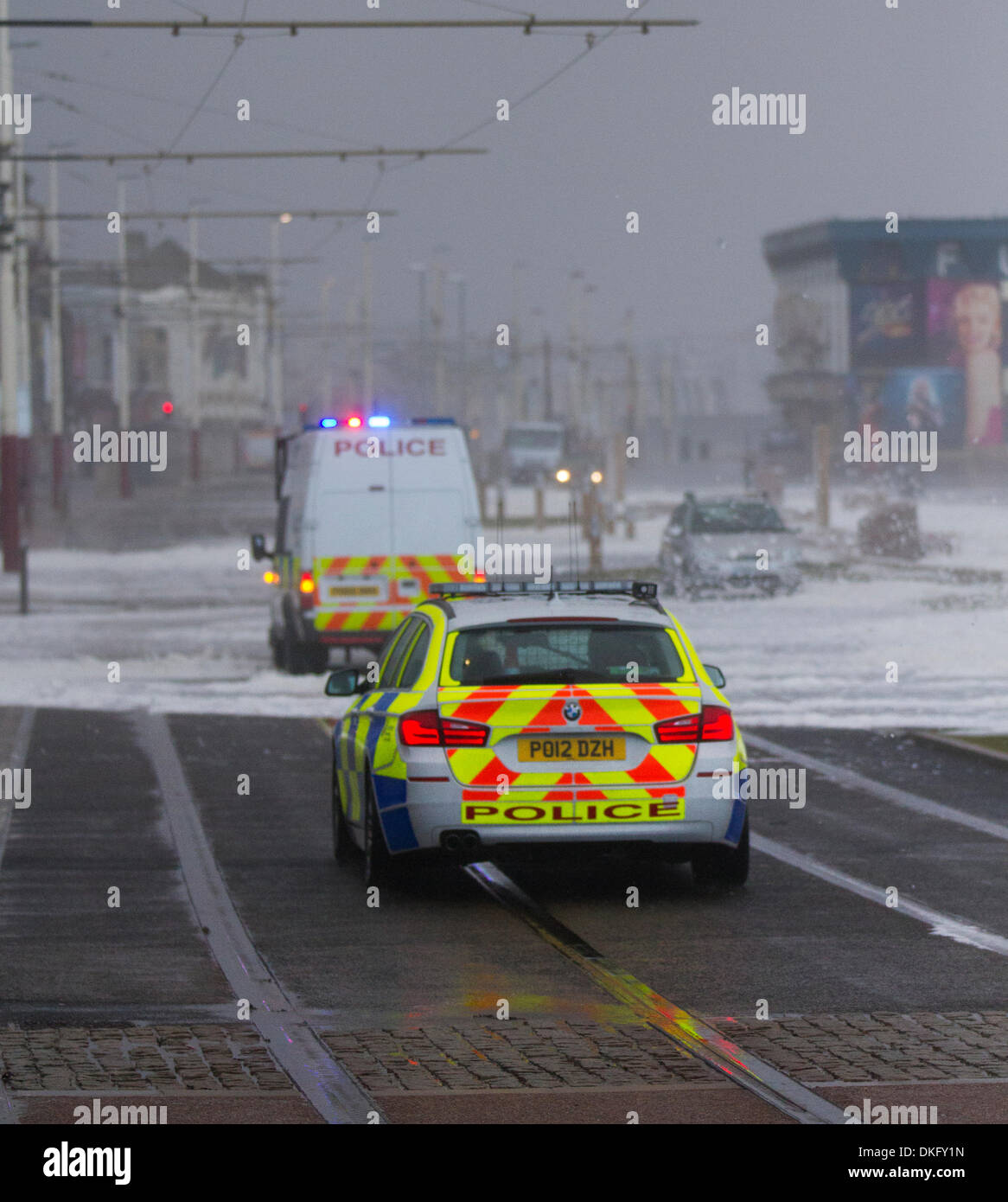 Blackpool, Lancashire, Regno Unito il 5 dicembre, 2013. Extreme UK Meteo. I veicoli della polizia di fronte al mare in tempesta schiumatura di sovratensioni mari e venti forti e alta marea a chiusura di forza di Promenade di Blackpool per veicoli e pedoni come venti alti e di allagamento distrugge la città. "Storm sovratensioni iniziano quando un aumento dell'area di bassa pressione impiega la pressione sulla superficie del mare, consentendo "rigonfiamento" verso l'alto, come che tira via, è possibile ottenere le condizioni di vento forte sul bordo posteriore della bassa pressione e quindi che fotte che il rigonfiamento di alto livello del mare verso il basso attraverso il Mare del Nord.' © Mar fotografico/Alamy Live Foto Stock