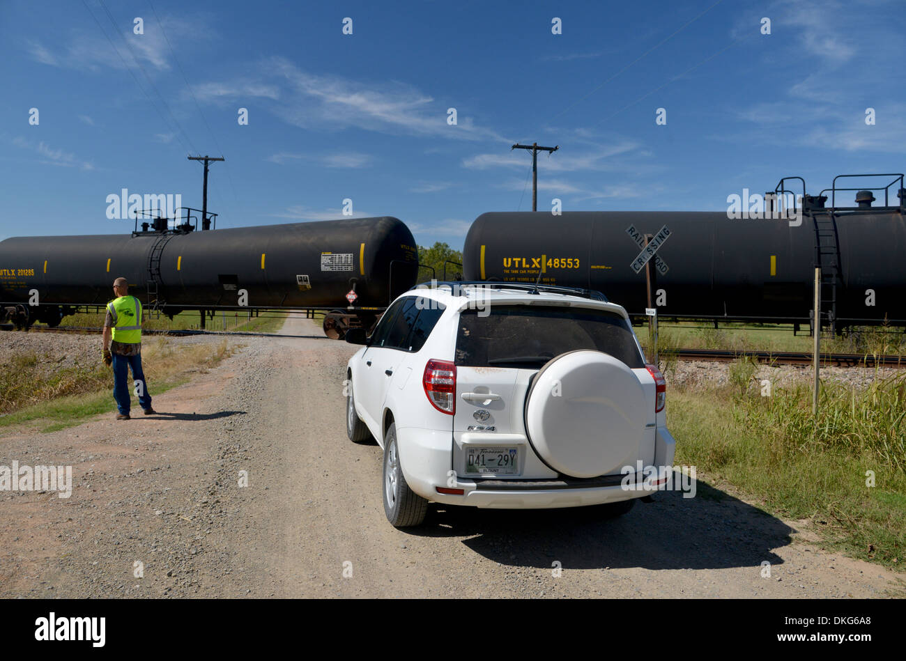 Auto in attesa a un attraversamento ferroviario sulla vecchia strada 66 strada sterrata mentre un interminabile tanker Treno auto accompagnate Foto Stock