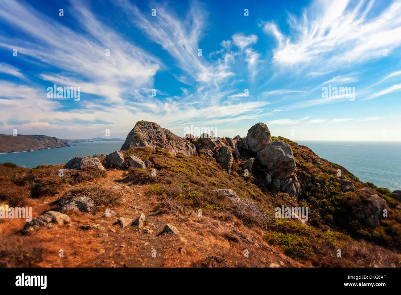 Una piccola figura onde la distanza che si affaccia su un paesaggio marino roccioso sulla costa della California in un drammatico cielo blu con nuvole Foto Stock
