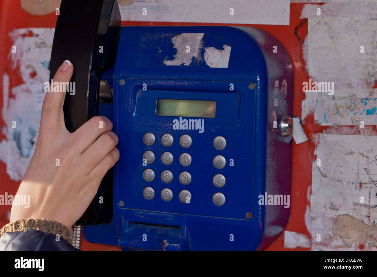 Donna che utilizza un telefono pubblico di raggiungere con la sua mano per prendere il ricevitore spento la culla Foto Stock