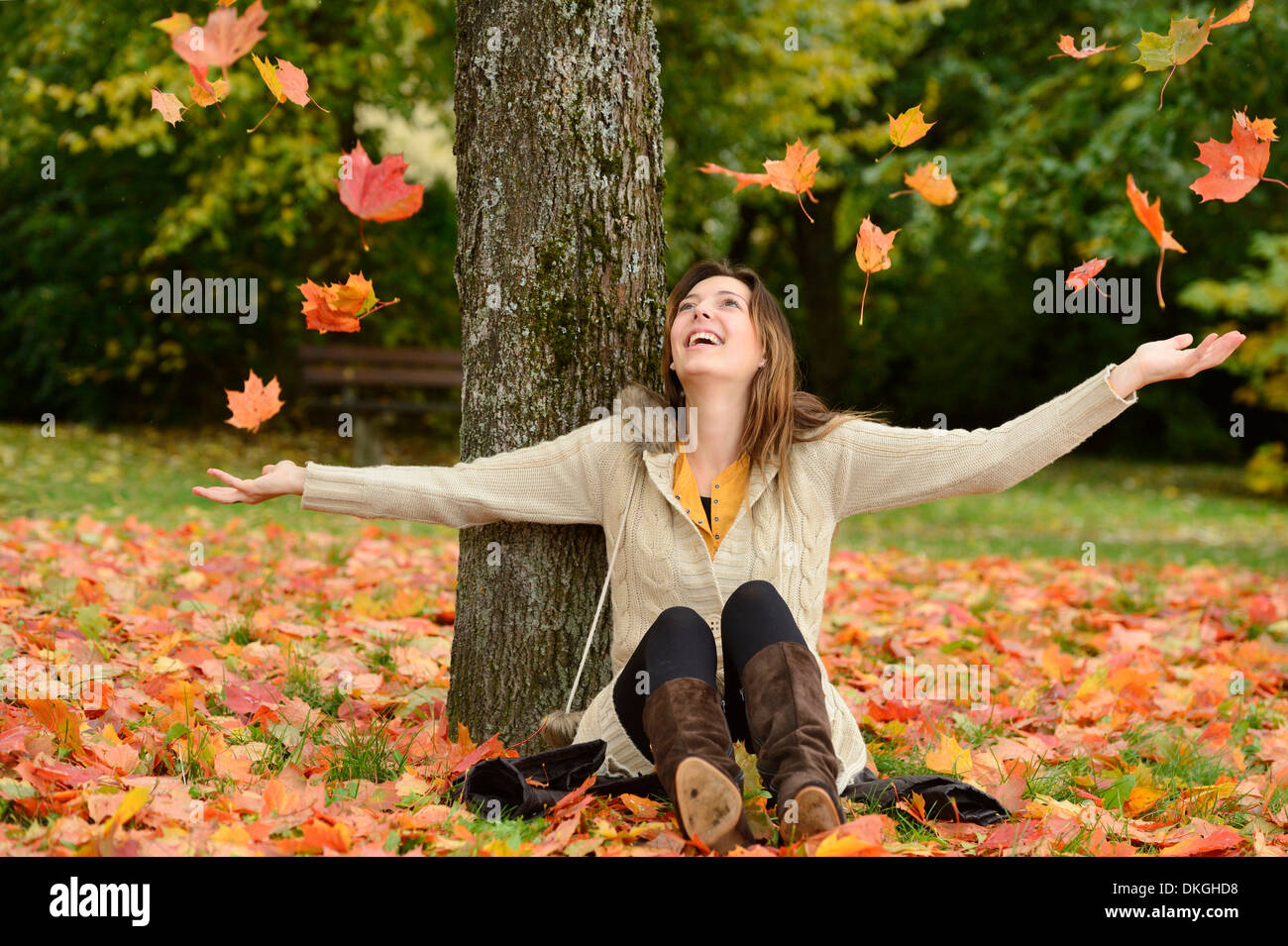 Felice giovane donna seduta sotto un albero in autunno Foto Stock