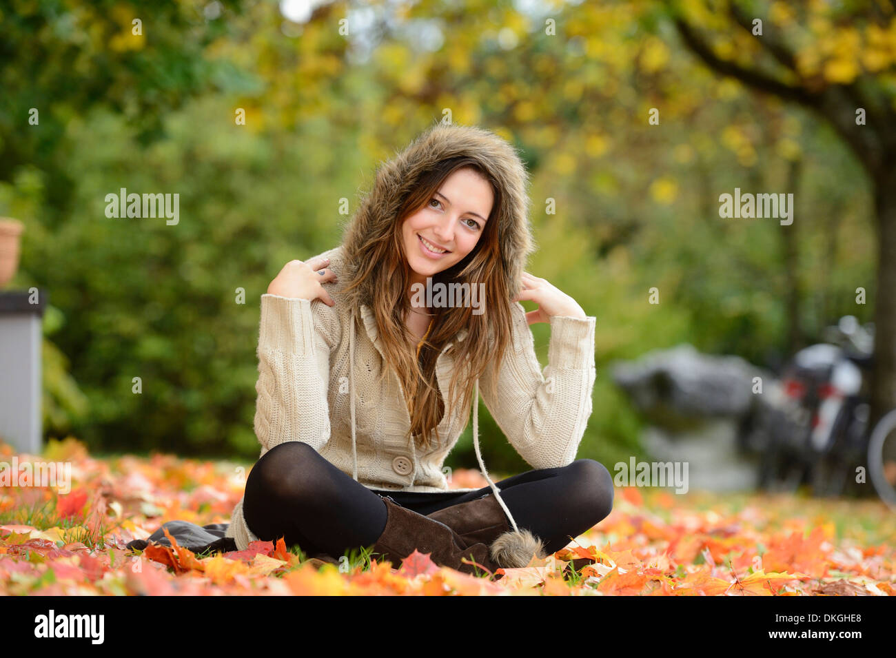 Sorridente giovane donna seduta in foglie di autunno Foto Stock