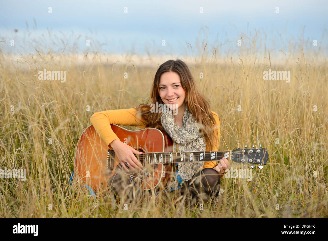 Sorridente giovane donna a suonare la chitarra nel campo Foto Stock