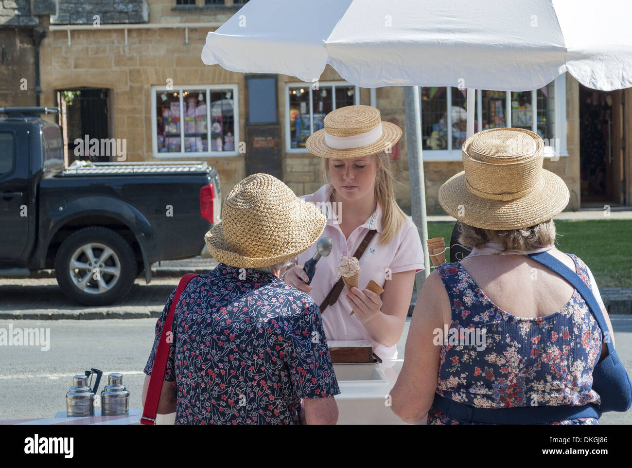 Ragazza di servire il gelato in una calda giornata estiva a due signore in paglia cappelli estivi nel villaggio di Broadway, Cotswold, England, Regno Unito Foto Stock