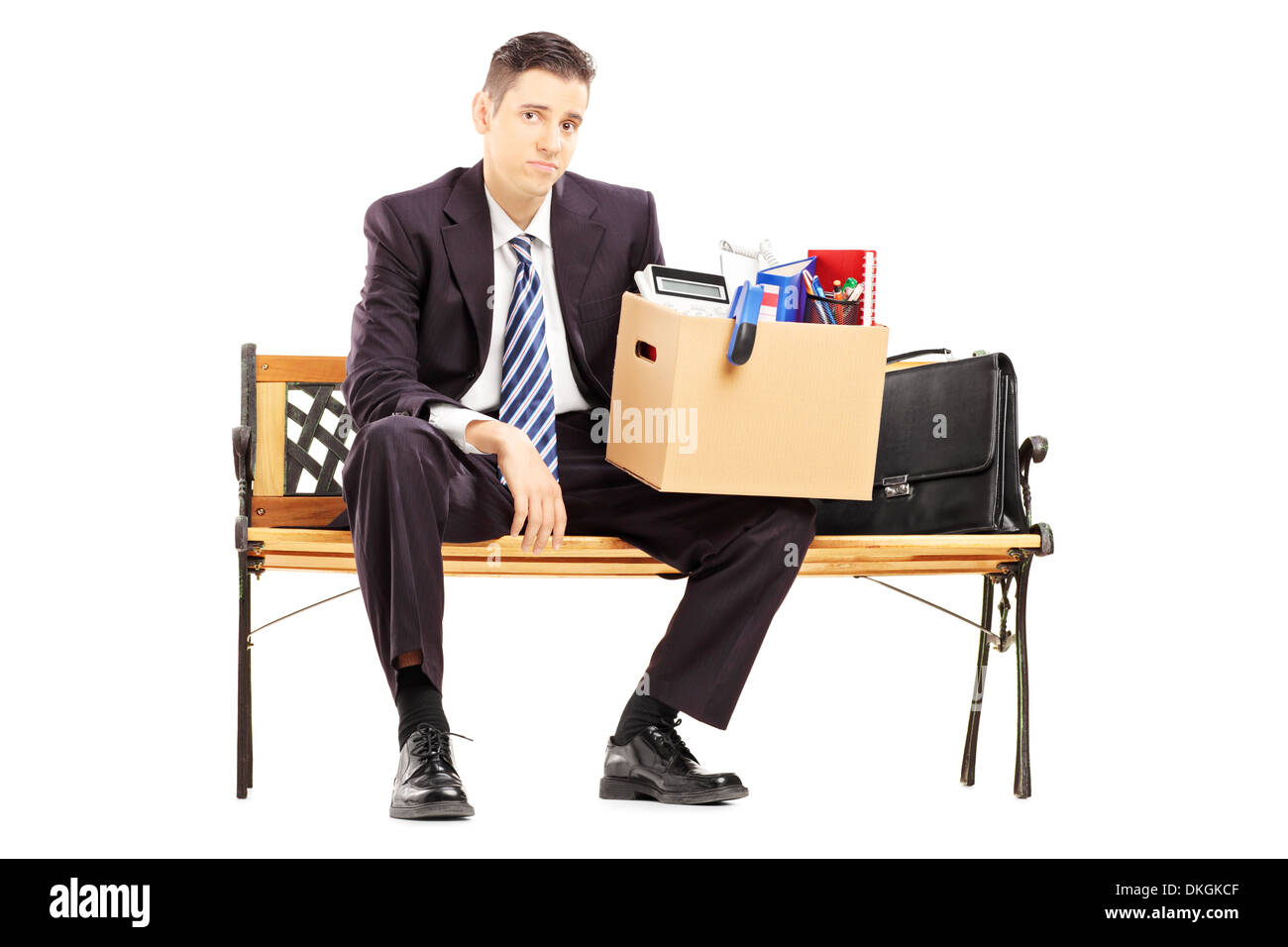 Deluso imprenditore ridondante in abito nero seduta su una panchina con una scatola di oggetti personali Foto Stock