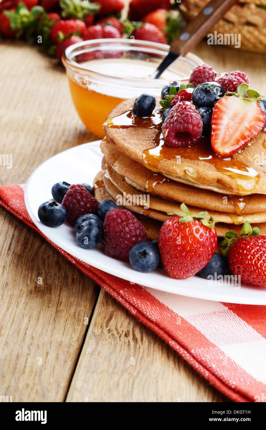 Piastra di colore bianco pieno di pancake con Fragole Lamponi Mirtilli e miele Foto Stock
