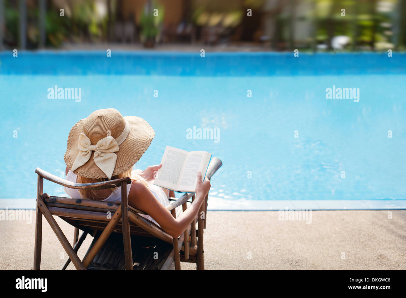 Donna leggere e rilassarsi vicino alla piscina di lusso Foto Stock