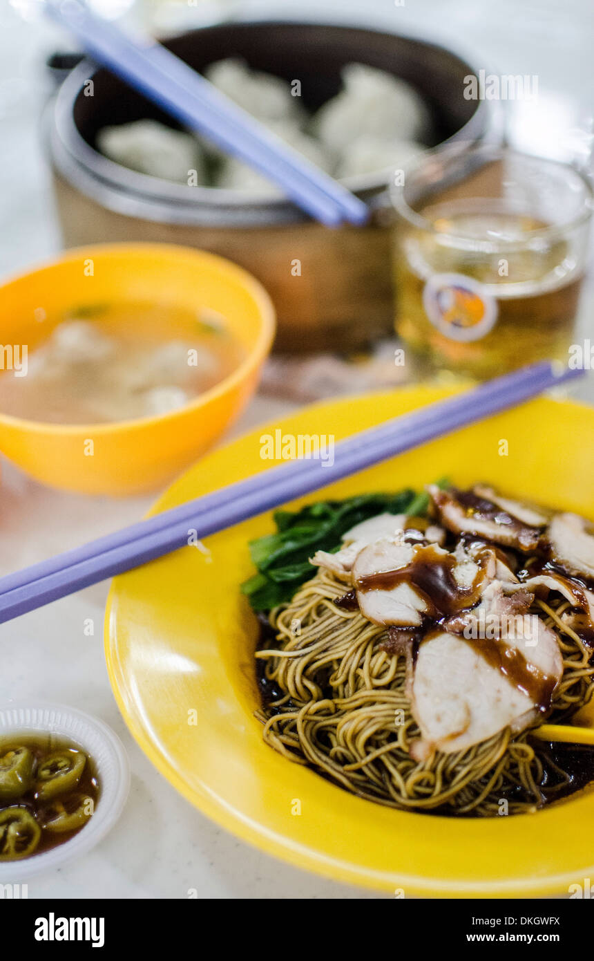 La carne di maiale tagliatelle (mee), servito con peperoncini sott'aceto, un brodo, i wonton e birra a Taman Dessa food court, Kuala Lumpur, Malesia Foto Stock