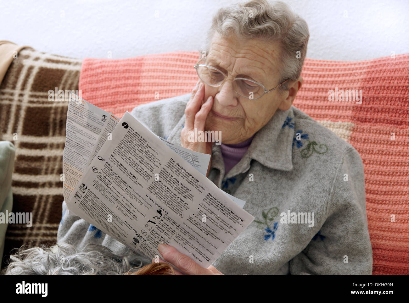 Donna anziana che indossa una giacca di lana guardando l'elettricità e gas bollette preoccupato per il costante aumento dei prezzi Foto Stock