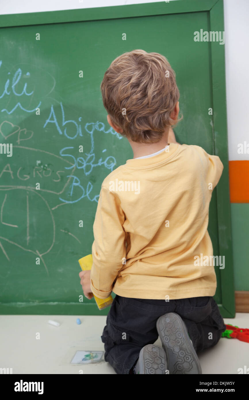 Ragazzo scrivere sulla lavagna a Kindergarten Foto Stock