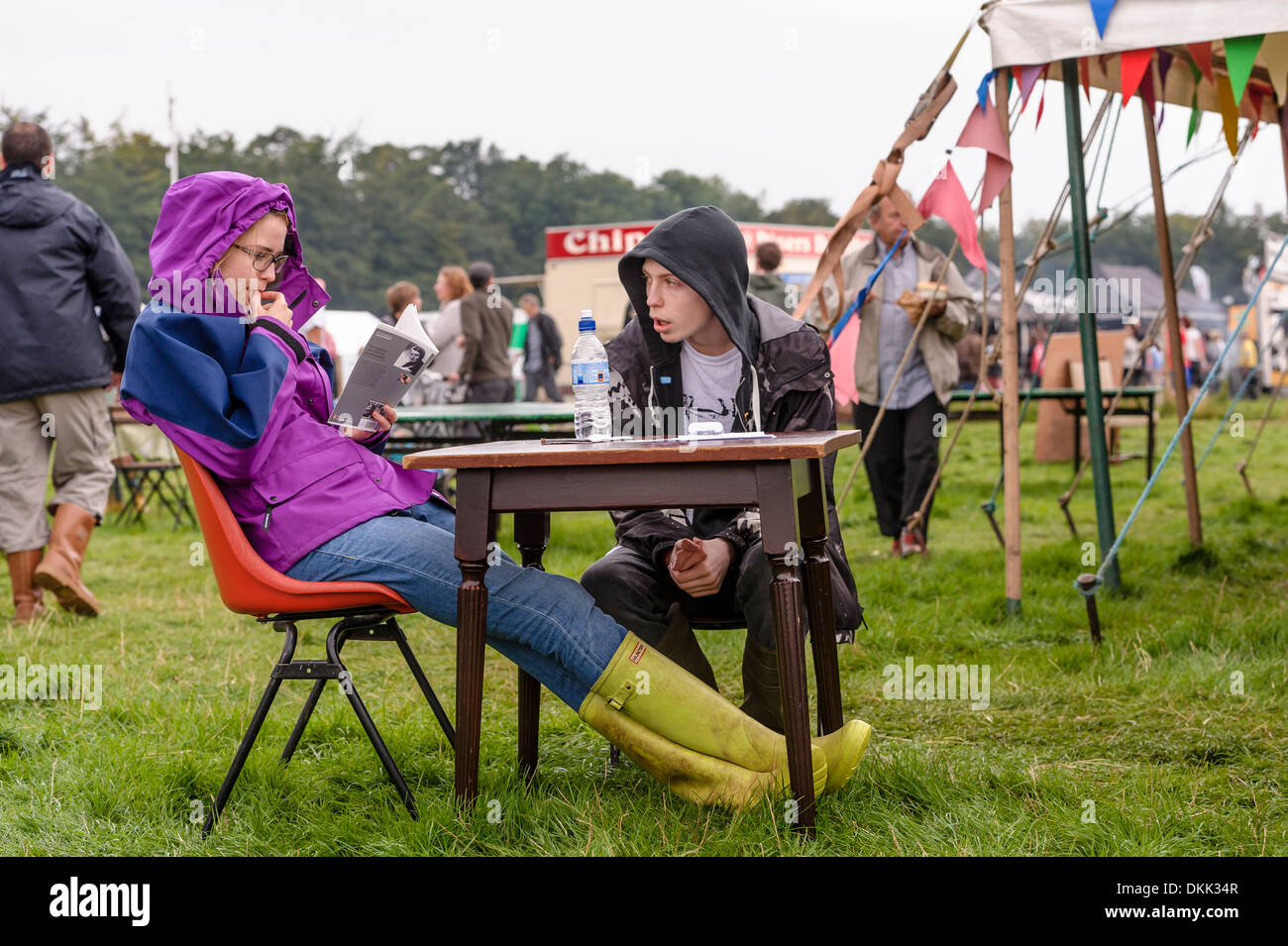 Un giovane si sedette ad un tavolo all'aperto presso un festival di musica. La giovane donna è la lettura. Foto Stock