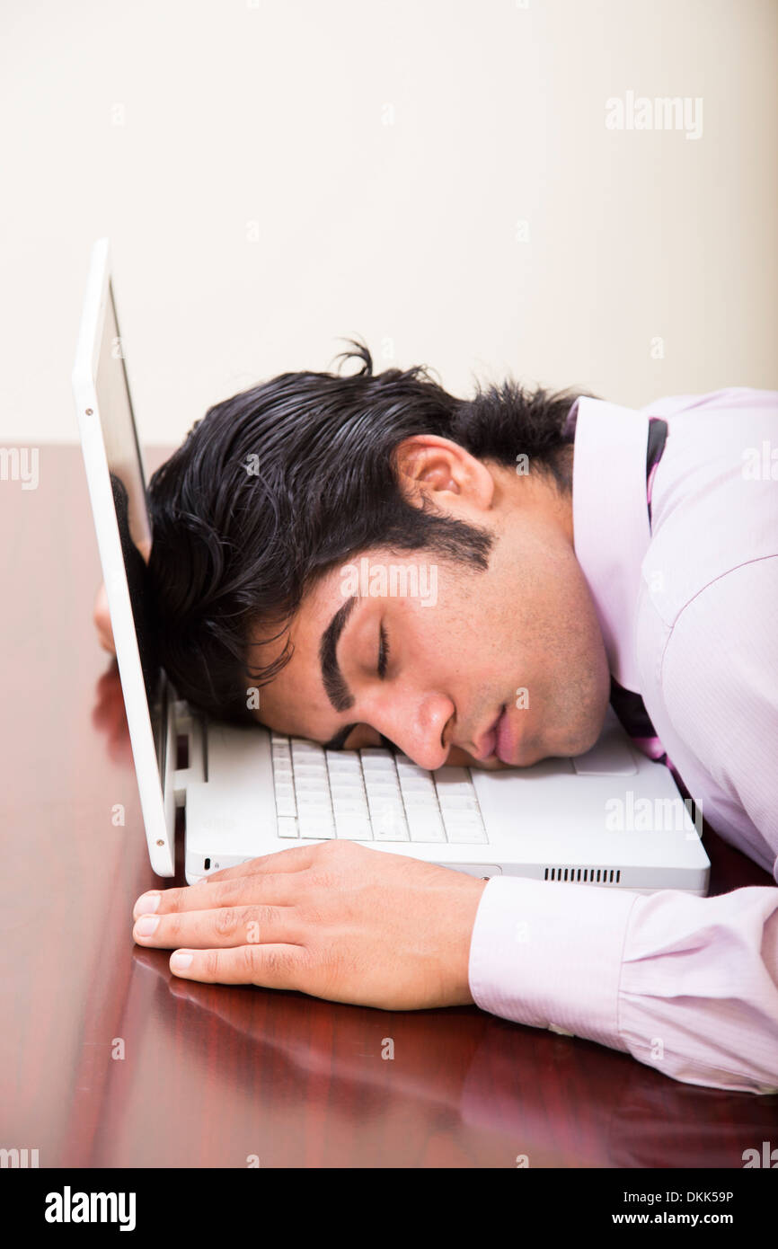 Giovani indiani uomo addormentato sul suo computer sul posto di lavoro Foto Stock