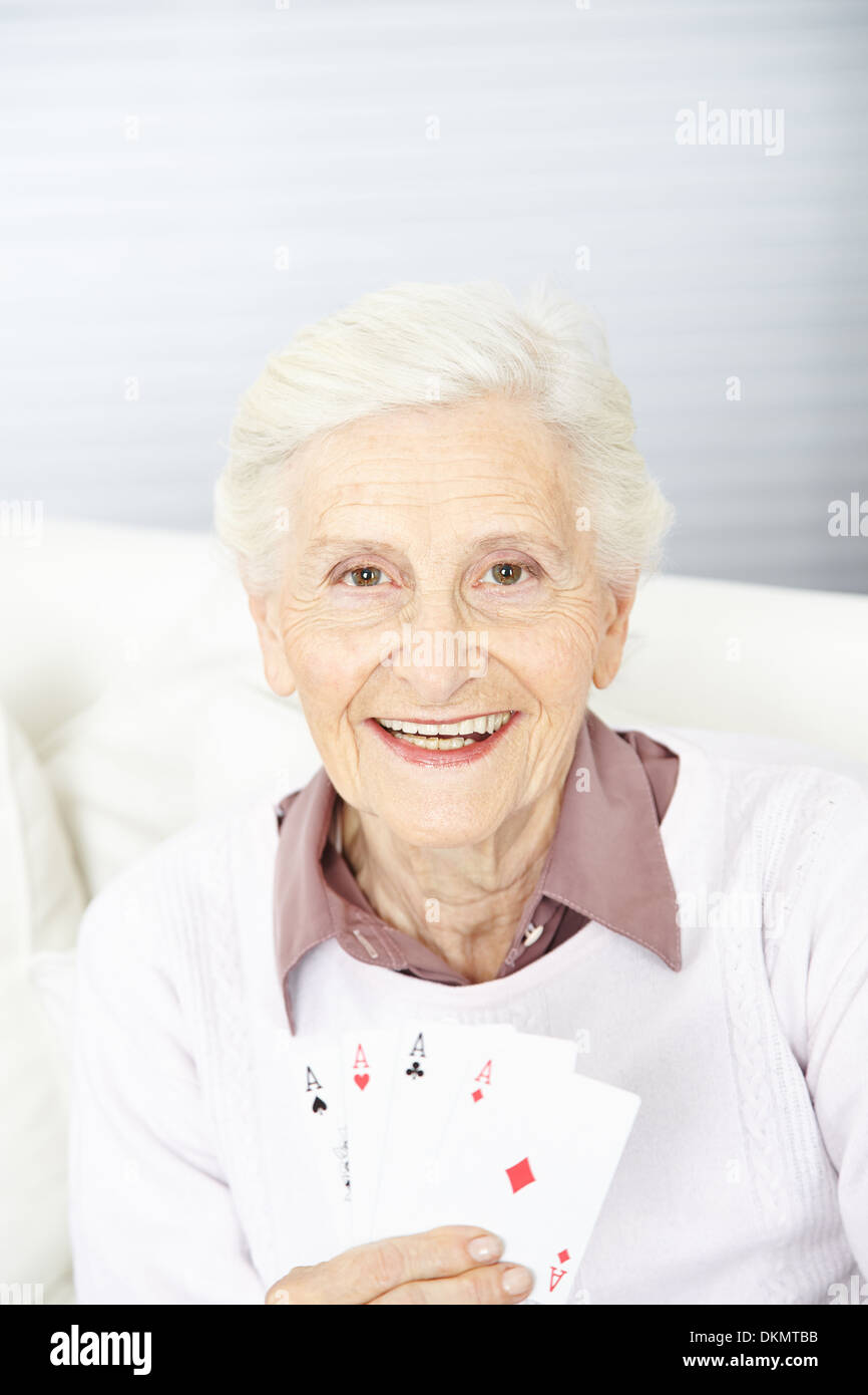 Sorridente donna senior azienda quattro assi in mano mentre le carte da gioco Foto Stock