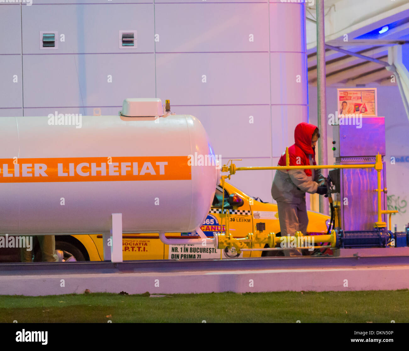 Lukoil gas station - Donna operatore effettua il rifornimento di carburante a GPL Dacia Logan taxi a Bucarest, Romania Foto Stock