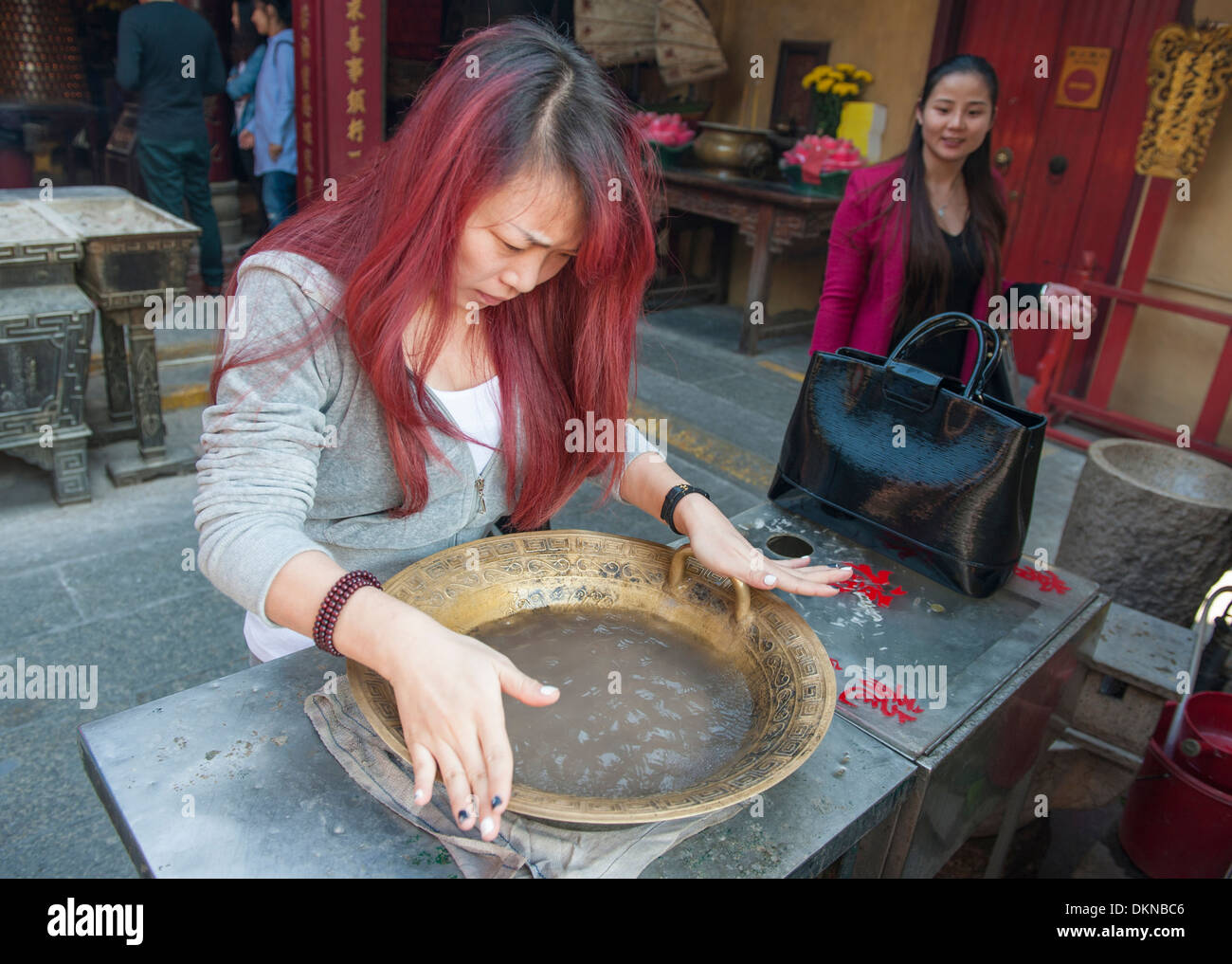 La donna lo sfregamento delle maniglie di un bronzo cinese ciotola di guarigione per un rituale di purificazione a Taoista del Tempio A-Ma, Macao, Cina Foto Stock
