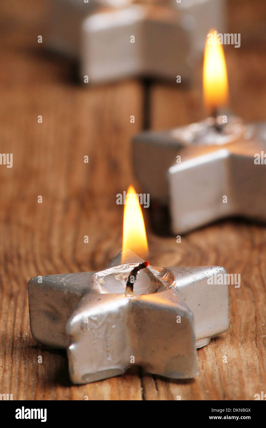 La masterizzazione a forma di stella candela sul vecchio legno stagionato con due candele in soft focus dietro Foto Stock