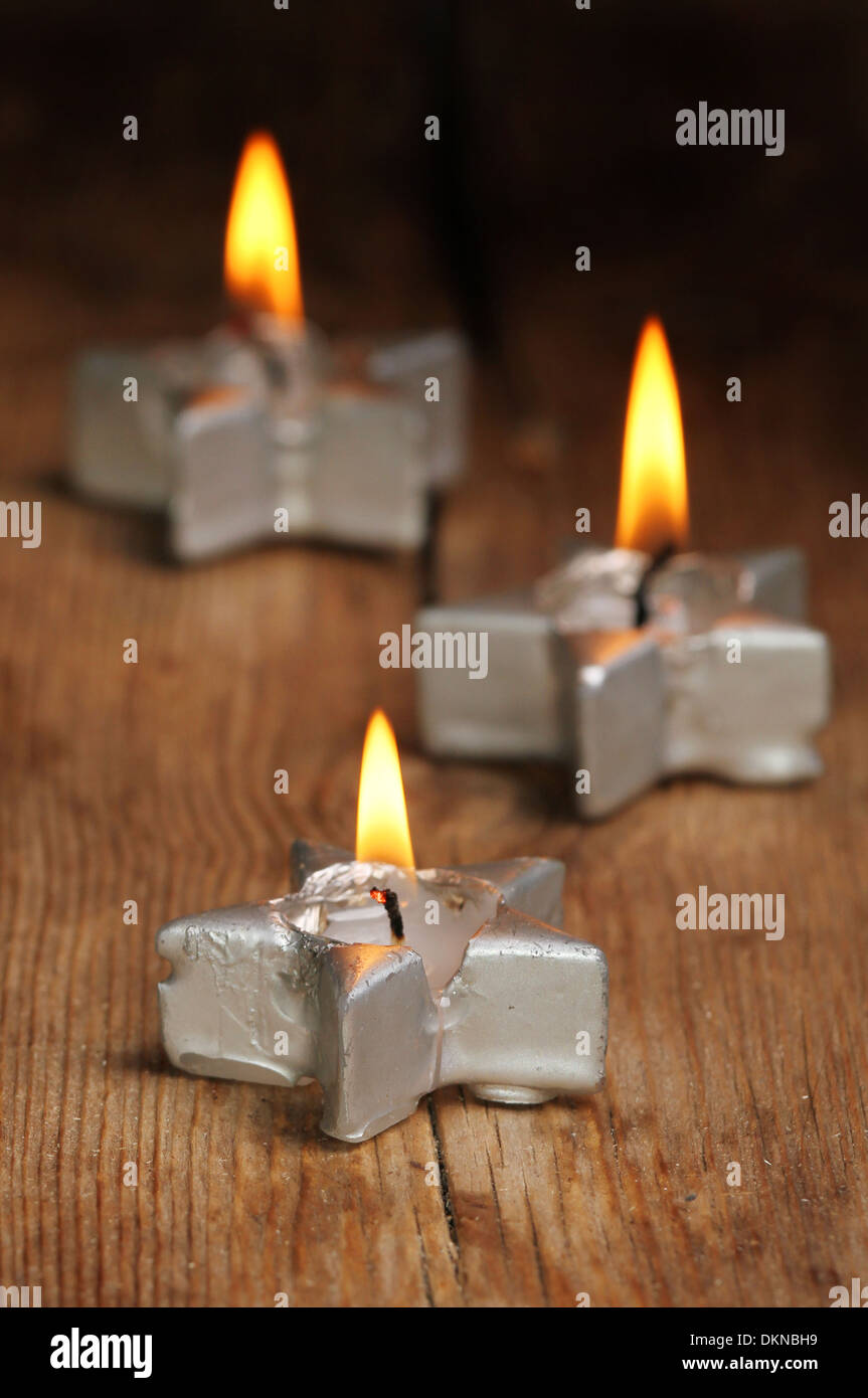 La masterizzazione di argento a forma di stella candela con due altri dietro in soft focus sul vecchio legno stagionato Foto Stock