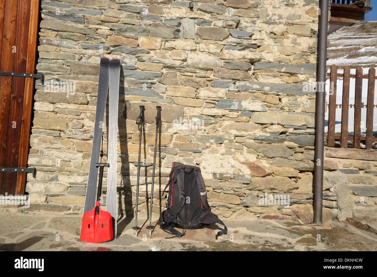 Coppia di sci tour con zaino e luce per la pala di salvataggio in caso di valanghe sul vecchio muro di pietra del rifugio alpino delle Alpi italiane Foto Stock