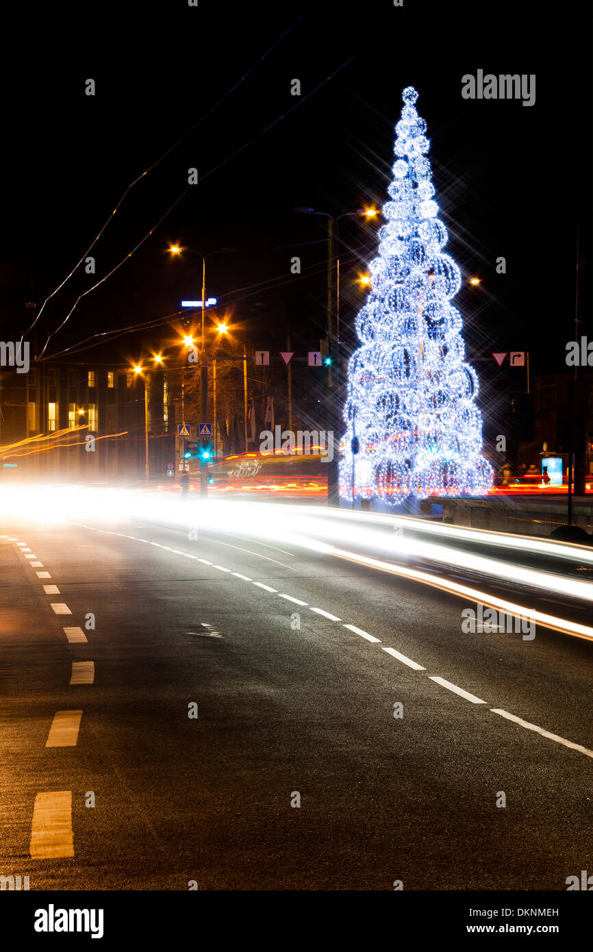 Illuminato albero di Natale fatto di cerchi rotondo nel mezzo di un veicolo street. Auto sentieri di luce in primo piano. Foto Stock