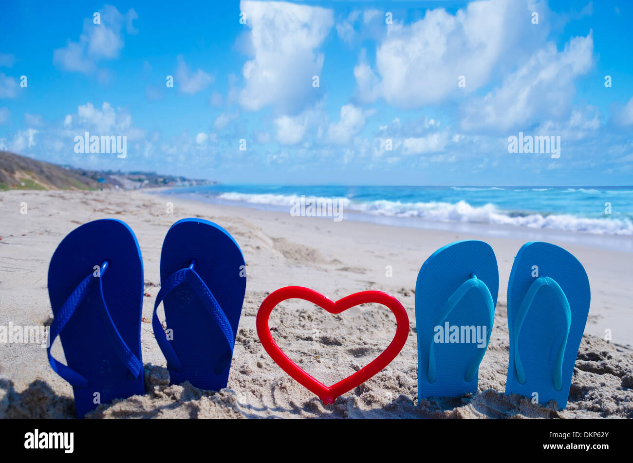Il flip flop a forma di cuore sulla spiaggia sabbiosa dall'oceano Foto Stock