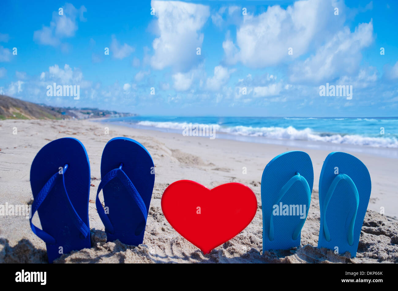 Il flip flop a forma di cuore sulla spiaggia sabbiosa dall'oceano Foto Stock